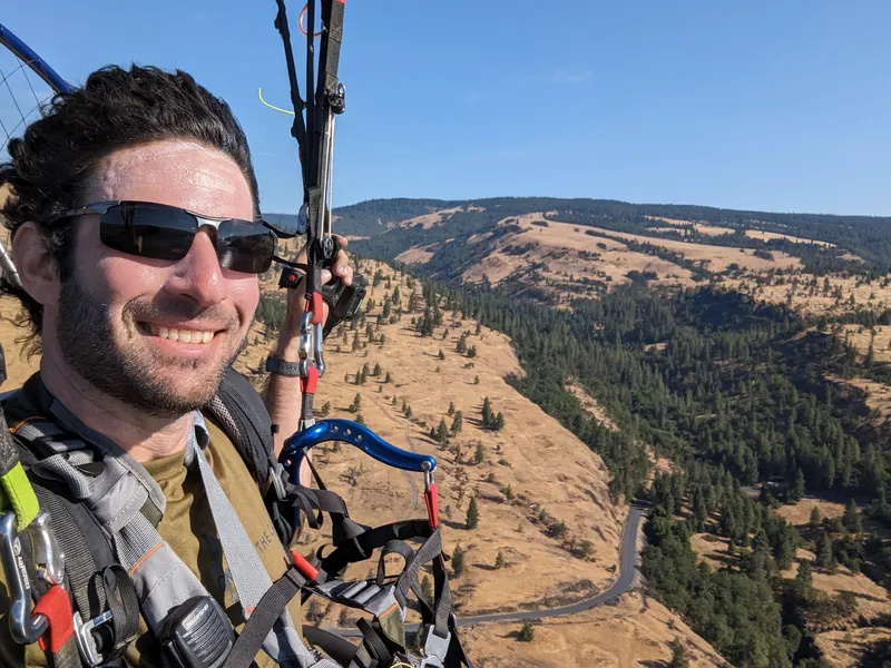 Nimo smiling in flight over golden hills and pine forest